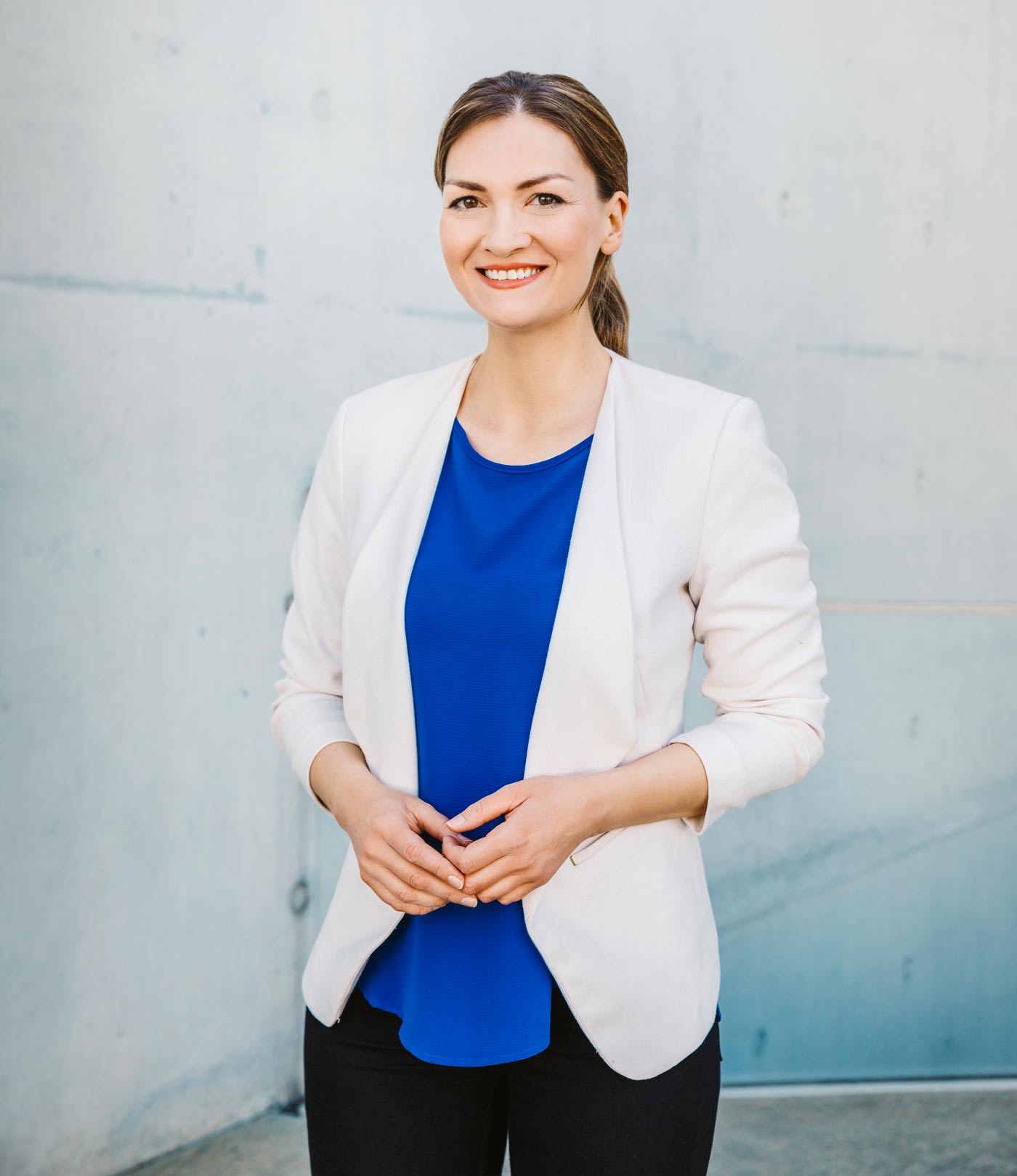 Die Bayerische Staatsministerin für Digitales, Judith Gerlach, in einem weißen Jacket und einem blauen T-Shirt lächelnd vor einer hellen Steinwand.